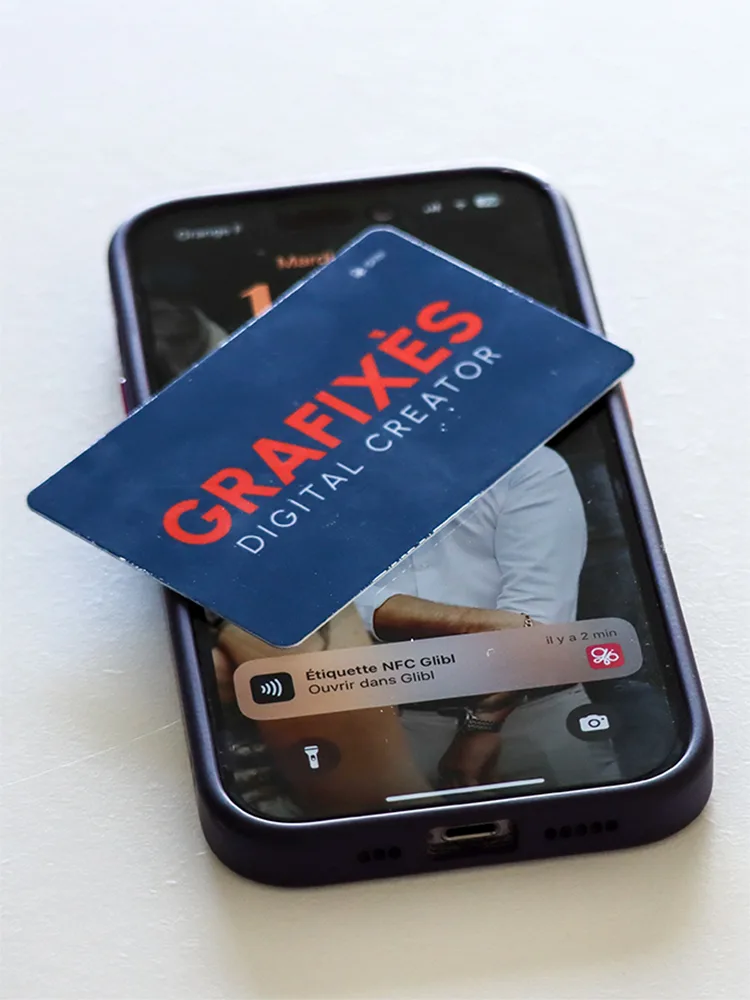 Image d'une carte NFC Grafixès posée sur un téléphone mobile, illustrant la technologie de carte de visite numérique. Cette carte permet de partager facilement les informations de contact sans contact physique.